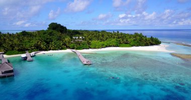 Maldivler 'de ağaç ve binaları olan bir adanın yanındaki tekneli turkuaz suyun havadan görüntüsü.