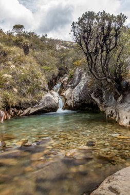 Parlak gün ışığında dağda küçük bir gölet ve şelale manzarası.