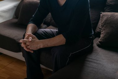 Yapayalnız bir adam, elleri kanepede bağlı oturuyor.