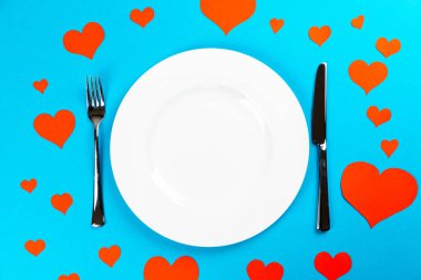 Mavi arka planlı beyaz bir plaka ve sevgililer günü yemeği için kırmızı kalpler.