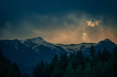 Ormanın yakınındaki karlı dağların üzerinde fırtınalı, karanlık bir gökyüzü.
