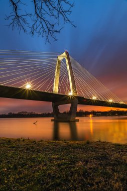 Gün batımında suyun üzerindeki köprünün dikey görüntüsü ve ufukta mavi bulutlu bir gökyüzü.