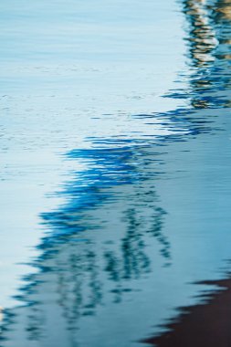 Mavi ve beyaz bir tekneyi yansıtan bir denizin dikey görüntüsü.