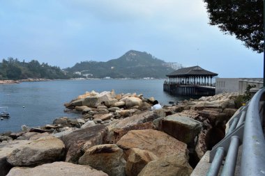 Hong Kong 'daki mavi deniz manzarası ve dağlara karşı kayalık bir kıyı manzarası.