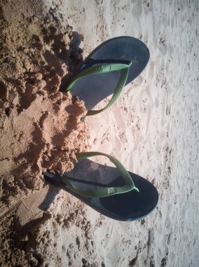 Güneşli bir günde kumsalda parmak arası terliklerin dikey çekimi