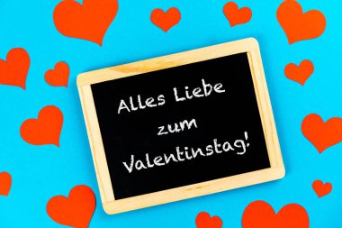 Sevgililer Günü için Alman metniyle mavi arka planda kırmızı kalpli bir karatahtanın üst görüntüsü.