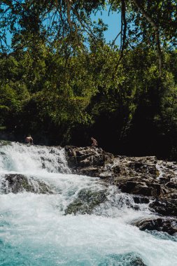 Küçük bir şelalenin yakınındaki kayalıklardaki insanların dikey görüntüsü