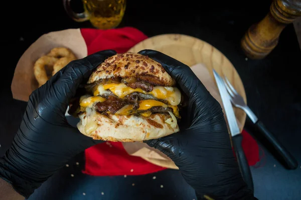 Siyah lastik eldivenli bir adamın elleri lezzetli bir burger tutuyor.