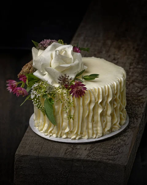 木製の板の上に花で飾られた豪華な小さなウェディングケーキの垂直ショット — ストック写真