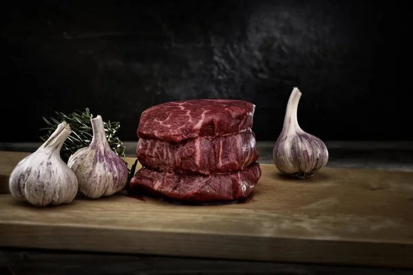 厚肉のステーキ肉とニンニクとローズマリーを木の板の上で新鮮なスライスで撮影した磁気クローズアップスタジオ — ストック写真