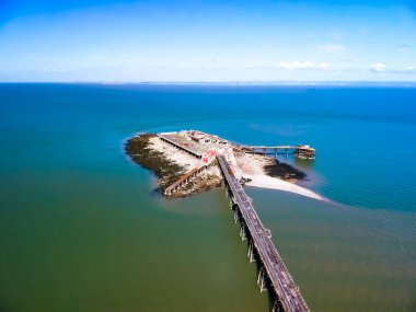 Deniz manzaralı bir iskele, ufukta açık mavi bir gökyüzü.