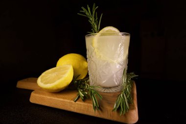 Biberiyeli limonlu cin toniğin yakın plan çekimi siyah arka planda izole edilmiş bir kesim tahtasının üzerinde.