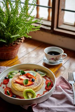 Meyveli güzel bir gözleme manzarası ve ev bitkisiyle çevrili bir masanın üzerinde bir fincan kahve.