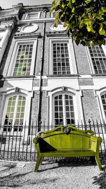Londra 'daki Hampton Court Sarayı' nın siyah ve beyaz manzarasında bir ağaç ve yeşil bankın dikey çekimi.