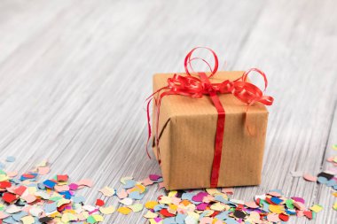 Tahta bir yüzey üzerinde paketlenmiş bir hediye kutusu, konfeti ve kurdeleler.