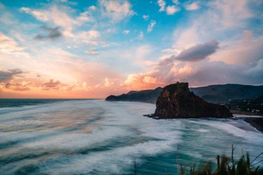 Alacakaranlık gökyüzü, Piha Sahili, Auckland, Yeni Zelanda 'ya karşı kaya oluşumunun ve dağların güzel manzarası.