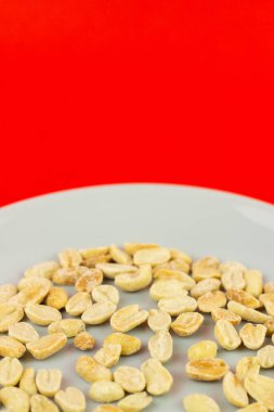 Kırmızı bir yüzey üzerinde tuzlanmış fıstık tabağının dikey yakın çekimi.