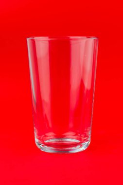 Kırmızı zemin üzerinde izole edilmiş boş bir bardağın dikey yakın çekimi