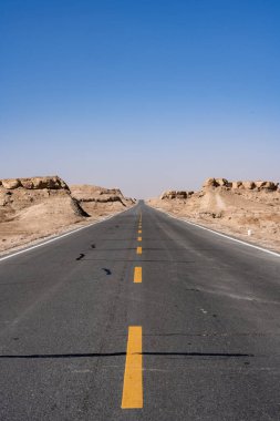 Gökyüzünün altındaki kayaların arasında boş bir otoyolun dikey görüntüsü.