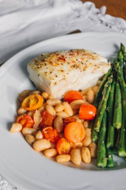 Kızarmış balık ve sebze. Akşam yemeği kuşkonmaz. Beyaz tabak üzerinde beyaz fasulye.