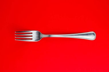 Parlak kırmızı arkaplanda gümüş bir çatalın üst görüntüsü..