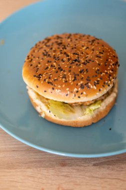 Masadaki mavi tabakta küçük bir hamburgerin dikey görüntüsü.