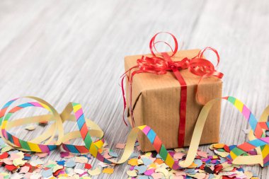 Tahta bir yüzey üzerinde paketlenmiş bir hediye kutusu, konfeti ve kurdeleler.