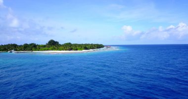 Maldivler 'de bulutlu gökyüzünün altında mavi denizi olan küçük yeşil bir adanın büyüleyici manzarası.