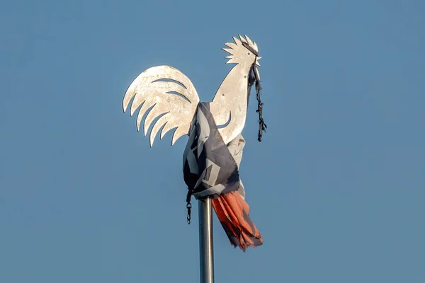 A closeup of a Rooster shaped metal weather vane with a cloth against clear blue sky