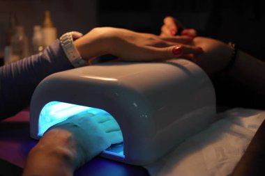 Kuaförde jel ojesini UV tırnak kurutma makinesiyle kurutan bir kadın.