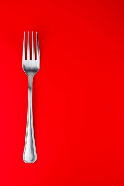 Parlak kırmızı arkaplanda gümüş çatalın dikey üst çekimi.