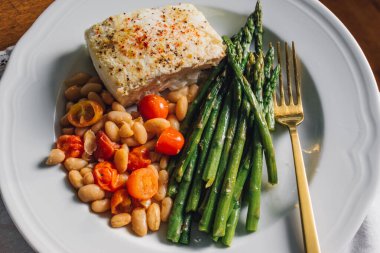 Kızarmış balık ve sebze. Akşam yemeği kuşkonmaz. Beyaz tabak üzerinde beyaz fasulye.