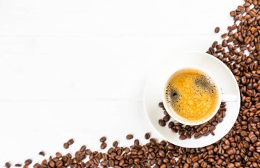 Kahve çekirdekli kahve fincanının üst görüntüsü beyaz ahşap arka planda izole edilmiş ve kopyalanmış.