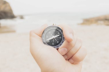 Kumlu bir kumsalda, bir adamın elinde benzer bir pusula tutarken çekilmiş yakın plan fotoğrafı.