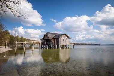 Almanya 'nın Bavyera kentindeki bulutlu gökyüzüne karşı Ammersee Gölü üzerinde güzel bir kayıkhane manzarası