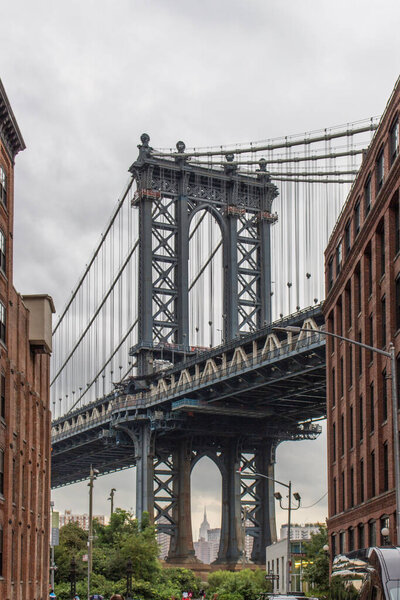 The Manhattan Bridge between two red brick buildings on a cloudy day in New York City, USA