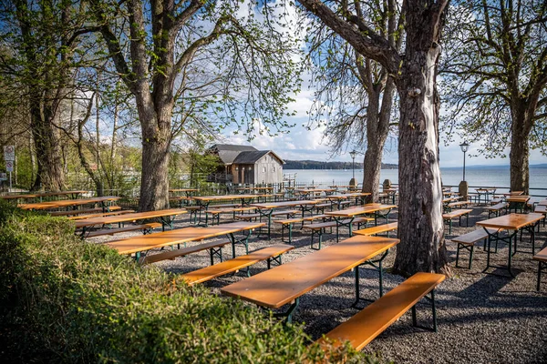 户外海滨咖啡馆的许多木制桌子和长椅 背景上有船屋和湖泊 — 图库照片