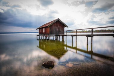 Almanya 'nın Bavyera kentindeki bulutlu gökyüzüne karşı Ammersee Gölü üzerinde güzel bir kayıkhane manzarası