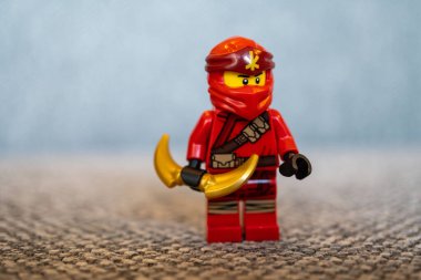 Bumerang tutan ve yerde duran kırmızı ninja elbiseli bir lego ninja oyuncak figürü.