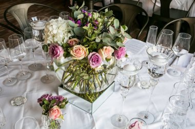 Restoranda gül ve gözlüklerle süslü bir masa manzarası.