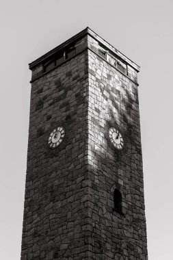 Duvarlarında saatler olan bir taş binanın dikey gri tonlu görüntüsü.