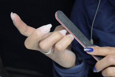 Bir kadının tırnaklarını tırnak törpüsüyle testereyle keserken çekilmiş yakın plan fotoğrafı.