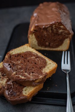 Geleneksel mermer kekin yakın plan fotoğrafı, ve gri bir masanın üzerindeki siyah tepside çatal ve bulanık arka plan.