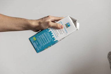 Reklam için beyaz duvara yapıştırılmış taze sütü tutan bir elin yakın çekimi.