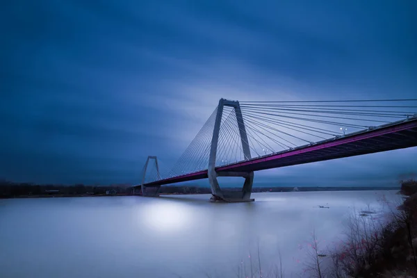 水平線の上の青い空と夜の間に水の上の橋の垂直ショット — ストック写真