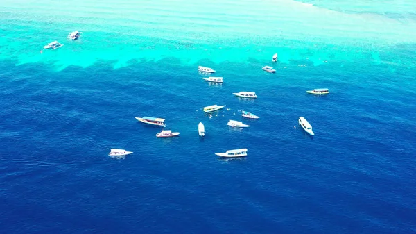 An aerial top view of yachts floating in turquoise water in the Maldives