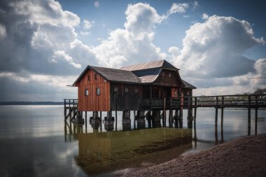 Almanya 'nın Bavyera kentindeki bulutlu gökyüzüne karşı Ammersee Gölü üzerinde güzel bir kayıkhane manzarası
