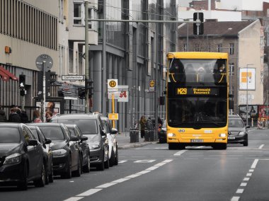 Berlin, Almanya 'da lüks arabaların yanında karşıdan karşıya geçen büyük sarı bir halk otobüsü.