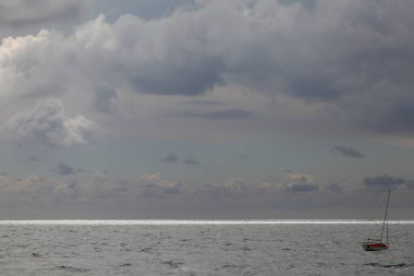 Bulutlu bir gökyüzüne karşı açık denizde bir yelkenli.