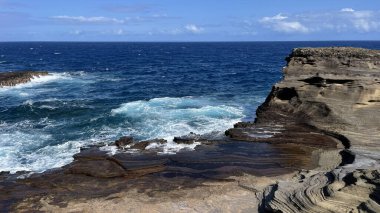 Güneşli bir havada kayalara vuran mavi okyanus dalgalarının manzarası.